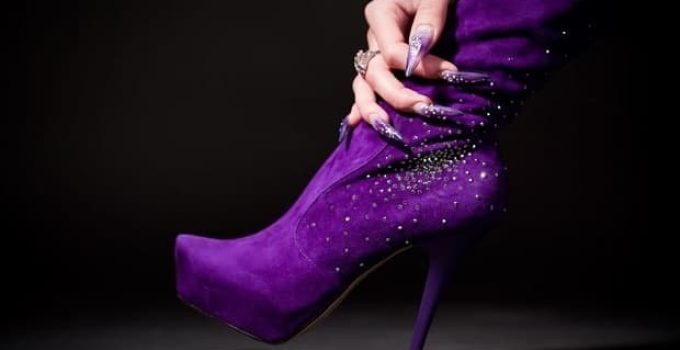 human hand with beautiful manicure hold purple boot. over black background suede boots