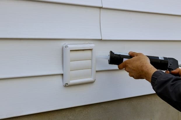 Man caulking outside clothes dryer vent cover