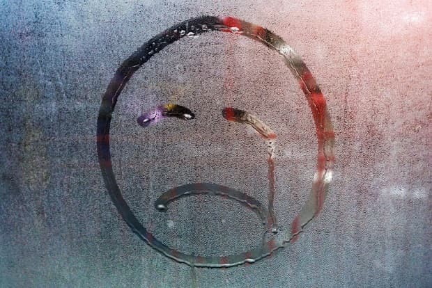 Wet home window with raindrops. Trees behind a wet window. Sad smiley of raindrops
